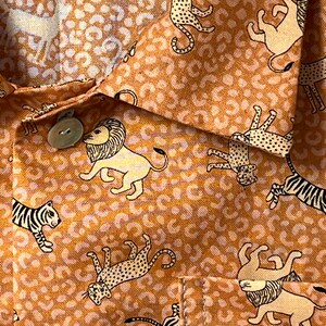 May include: A brown and beige fabric with a repeating pattern of stylized lions, tigers, and leopards. The fabric has a subtle texture and a slightly faded appearance.