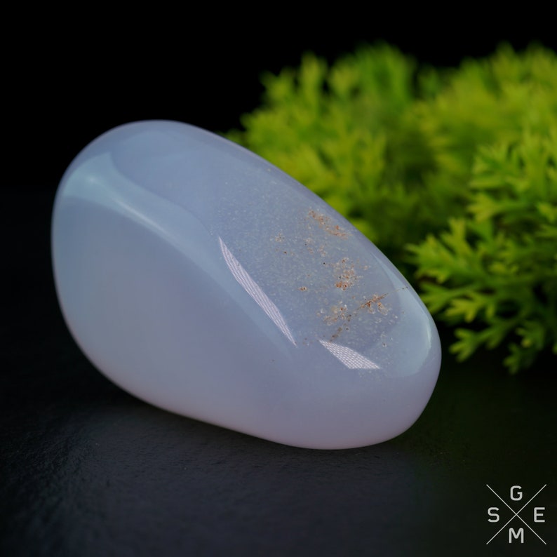 Pode incluir: Uma pedra de calced&ocirc;nia lisa de cor azul claro com uma forma arredondada oval. A pedra tem um padr&atilde;o sutil e salpicado de inclus&otilde;es de cor marrom claro.