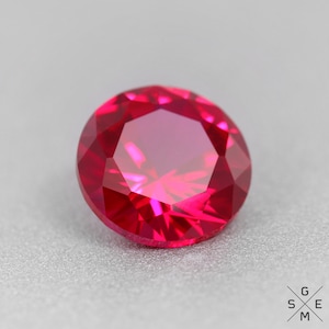 May include: A vibrant red ruby gemstone with a faceted cut. The gemstone is round and has a high polish.