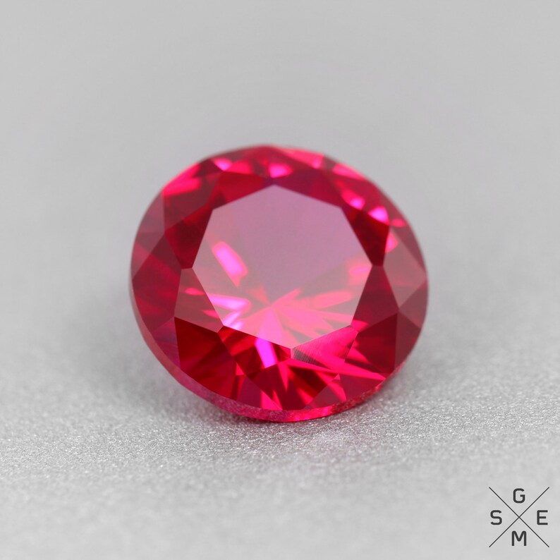 May include: A vibrant red ruby gemstone with a faceted cut. The gemstone is round and has a high polish.