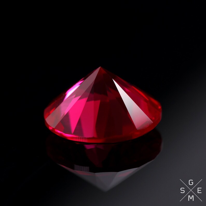 May include: A deep red ruby gemstone with a faceted cut, reflecting light against a black background.