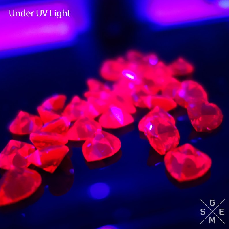 May include: A close-up of several small, heart-shaped, red gemstones under a UV light. The gemstones are glowing brightly in the dark.