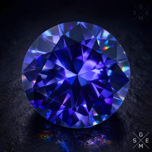 May include: A round, faceted gemstone with a deep blue hue. The gem's surface reflects light, creating a spectrum of colors. The gemstone is set against a dark background, highlighting its brilliance. The image includes the letters G, S, and E.