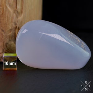 Pode incluir: Uma pedra de calced&ocirc;nia lisa de cor azul claro, em forma de l&aacute;grima, medindo aproximadamente 10 mm de comprimento. A pedra tem uma apar&ecirc;ncia ligeiramente nublada e &eacute; polida com alto brilho.