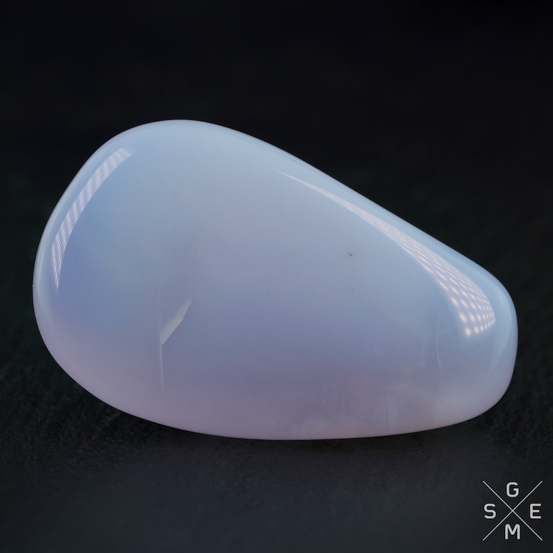 Pode incluir: Uma pedra de calced&ocirc;nia oval, lisa e de cor azul p&aacute;lida. A pedra tem uma apar&ecirc;ncia ligeiramente transl&uacute;cida e um brilho sutil.