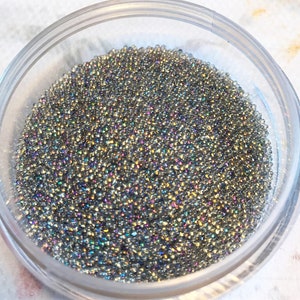 May include: A clear plastic container filled with iridescent silver micro beads. The beads are small and round, and they have a shimmery finish.