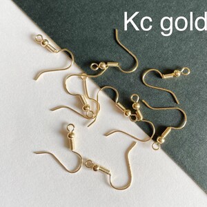 May include: A close-up of a group of gold-toned earring hooks. The hooks are arranged on a white surface with a black background. The text "Kc gold" is visible in the upper right corner of the image.