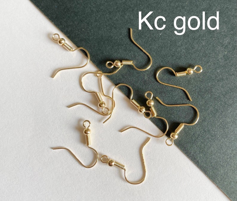 May include: A close-up of a group of gold-toned earring hooks. The hooks are arranged on a white surface with a black background. The text "Kc gold" is visible in the upper right corner of the image.