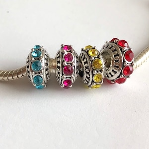 Op de afbeelding: Vier zilveren bedelarmbanden met verschillende gekleurde strass steentjes. De kralen zijn turquoise, roze, geel en rood.