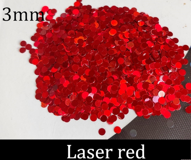Pu&ograve; includere: Un'immagine ravvicinata di glitter laser rosso da 3 mm. Il glitter ha la forma di piccoli cerchi rotondi.