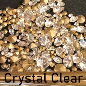 May include: A close-up image of a mix of clear and gold rhinestones. The rhinestones are scattered on a black surface. The text "Crystal Clear" is visible at the bottom of the image.