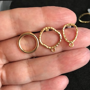 Op de afbeelding: Drie goudkleurige metalen springringen. De ringen zijn in verschillende maten en vormen. Eén is een eenvoudige cirkel, een andere is een licht ovale vorm en de derde is een onregelmatiger vorm met een getextureerd oppervlak.