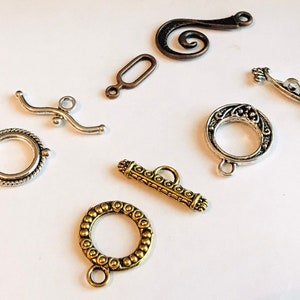 May include: Assortment of silver and gold tone metal clasps and connectors for jewelry making.  The clasps are in various shapes and sizes, including a circle, a rectangle, a curved bar, and a swirl.