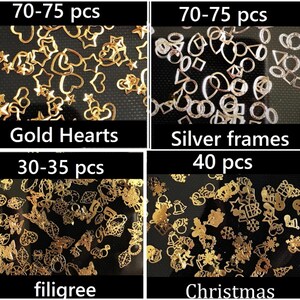 Op de afbeelding: Assortiment van gouden en zilveren nagelkunstcharms. De charms omvatten harten, sterren, frames, filigraan en kerstthema-ontwerpen. De afbeelding toont vier verschillende sets charms met de hoeveelheid van elke set.