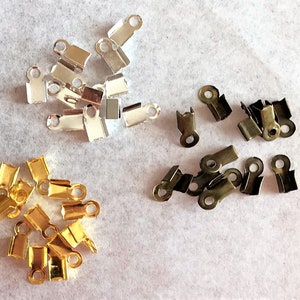 Op de afbeelding: Assortiment van metalen sluitingen in goud, zilver en brons. De sluitingen zijn klein en hebben aan de ene kant een lus en aan de andere kant een haak. Ze worden vaak gebruikt voor het maken van sieraden en andere knutselwerkjes.