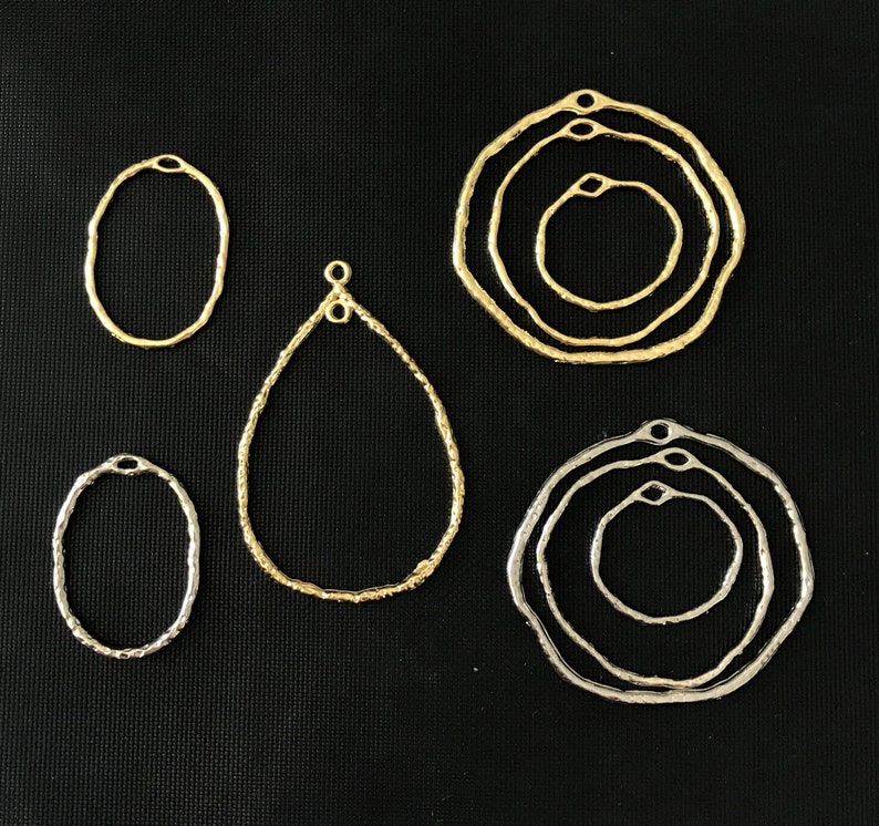 May include: Six gold and silver metal hoops with textured edges. The hoops are in various sizes and shapes, including circles, ovals, and teardrops.