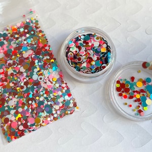 Pu&ograve; includere: Un contenitore di plastica trasparente pieno di glitter colorati iridescenti di diverse dimensioni e forme. Il glitter &egrave; un mix di rosso, rosa, blu, verde, oro e bianco.