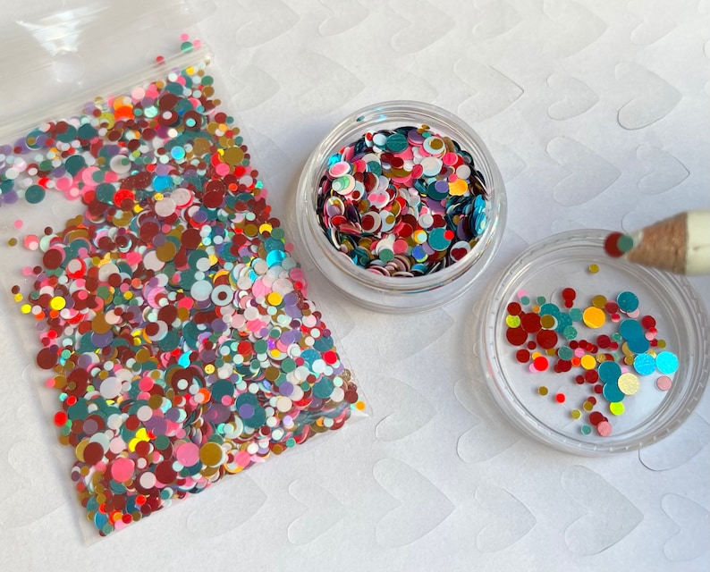 Pu&ograve; includere: Un contenitore di plastica trasparente pieno di glitter colorati iridescenti di diverse dimensioni e forme. Il glitter &egrave; un mix di rosso, rosa, blu, verde, oro e bianco.