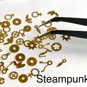 Op de afbeelding: Een verzameling van goudkleurige metalen tandwielen en horlogeonderdelen, sommige met ingewikkelde ontwerpen, gerangschikt op een wit oppervlak. Het woord "Steampunk" staat in zwarte letters onderaan de afbeelding.