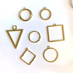 May include: A set of seven gold-toned metal pendant frames in various shapes, including a circle, square, triangle, and a diamond. The frames are all textured with a braided design.