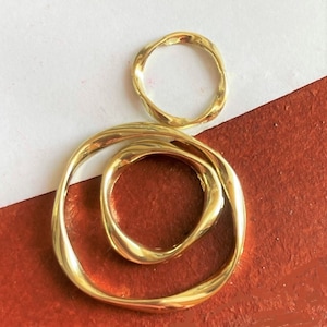 May include: Two gold rings, one larger than the other, are interlocked. The larger ring is thicker and has a more organic shape. The smaller ring is thinner and more circular.