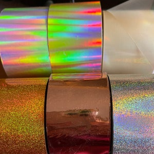 Op de afbeelding: Assortiment van iriserende en glitterklevende tape rollen. De rollen zijn in verschillende kleuren, waaronder goud, zilver en holografisch.