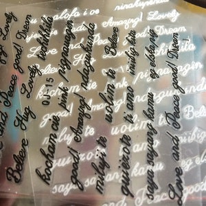 May include: A close-up of a sheet of clear plastic with various words and phrases printed on it in black ink. The words include "Love", "Peace", "Believe", "Amazing", "Hug", "Good", "Dream", "Kocham cie", "Miluji te", "Volim te", "Iniibig kita", "Saya sayang kamu", "Eg elska", "Niibig kita", and "Aloha i os".