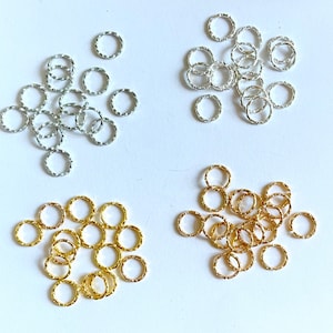 May include: Assortment of silver and gold jump rings. The jump rings are small and have a textured surface.