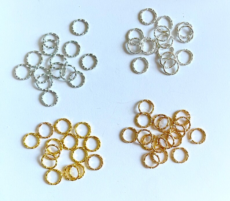 May include: Assortment of silver and gold jump rings. The jump rings are small and have a textured surface.