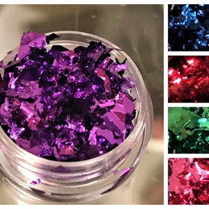 May include: A small clear jar filled with loose purple metallic flakes. The flakes are iridescent and have a shiny finish.