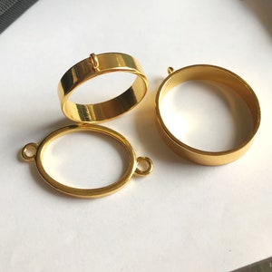 Könnte beinhalten: Drei goldfarbene Metallringrohlinge für die Schmuckherstellung. Die Rohlinge haben verschiedene Formen: ein runder Ring, ein ovaler Ring und ein kleiner runder Ring mit einer Schlaufe oben.