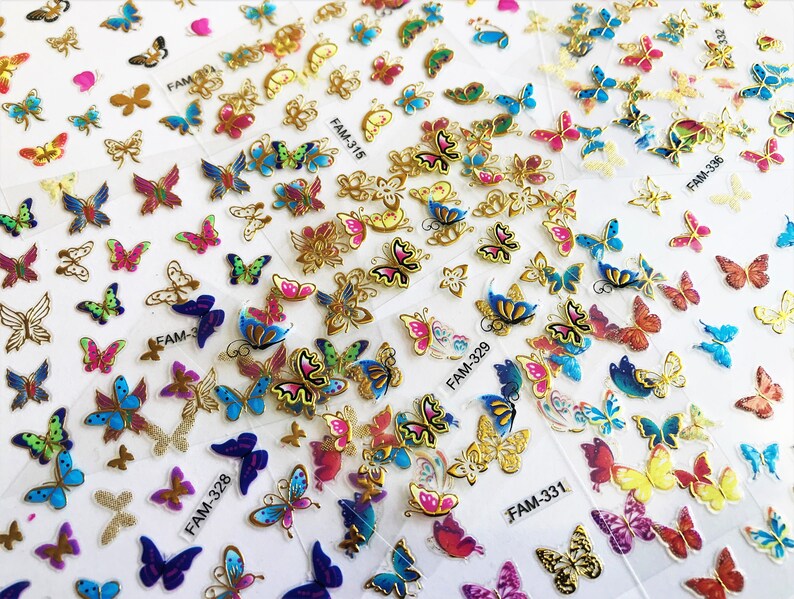 May include: Assortment of colorful butterfly nail art stickers. The stickers feature various butterfly designs with gold accents. The stickers are packaged on sheets labeled with the product code, such as "FAM-328" and "FAM-331".