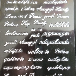 May include: A sheet of clear plastic with white lettering. The sheet contains various phrases in different languages, including "Love and Peace good! Dream", "Believe Hug Lovely", "kocham cie pink pigpauagin", "good! Amazing! ndagukunda", "miluji te volim te Believe", "quiezote ti amo iniibig kita", "saya sayang kamu eg elska pig", and "Love and Peace good! Dream".