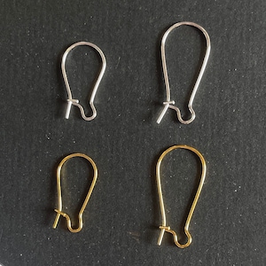Op de afbeelding: Vier oorhaken, twee zilver en twee goud. De haken zijn allemaal even groot en in dezelfde vorm, met een kleine lus bovenaan en een gebogen draad die een haak vormt.