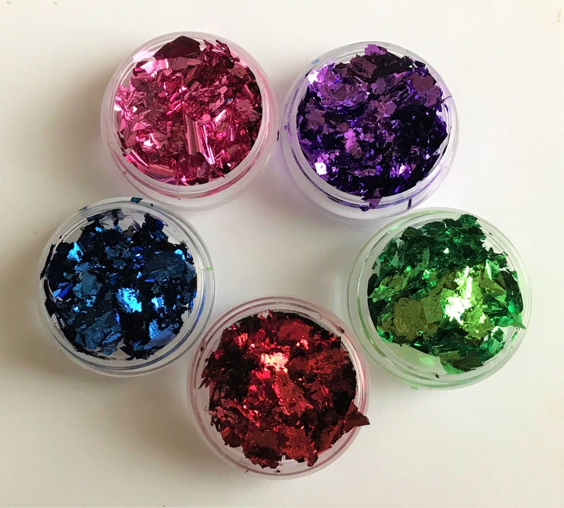 May include: Five small jars filled with colorful metallic flakes. The jars are clear plastic and the flakes are pink, purple, blue, green, and red.