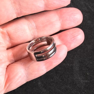 May include: A silver-colored ring with a modern design. The ring features three horizontal cut-out sections, creating a unique and open look. The ring is smooth and shiny, reflecting light.