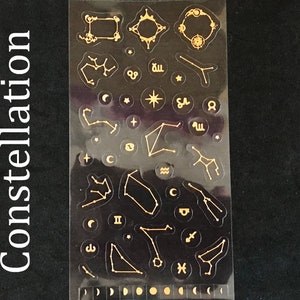 May include: A sheet of gold constellation stickers on a black background. The stickers feature various constellations, stars, and zodiac symbols.