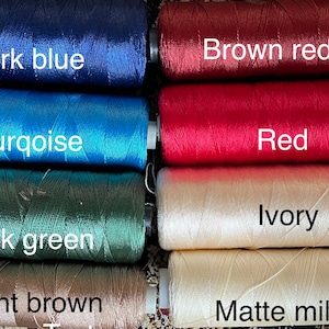 May include: Close-up of eight spools of thread in different colors. The colors are dark blue, turquoise, dark green, light brown, brown red, red, ivory, and matte milky.