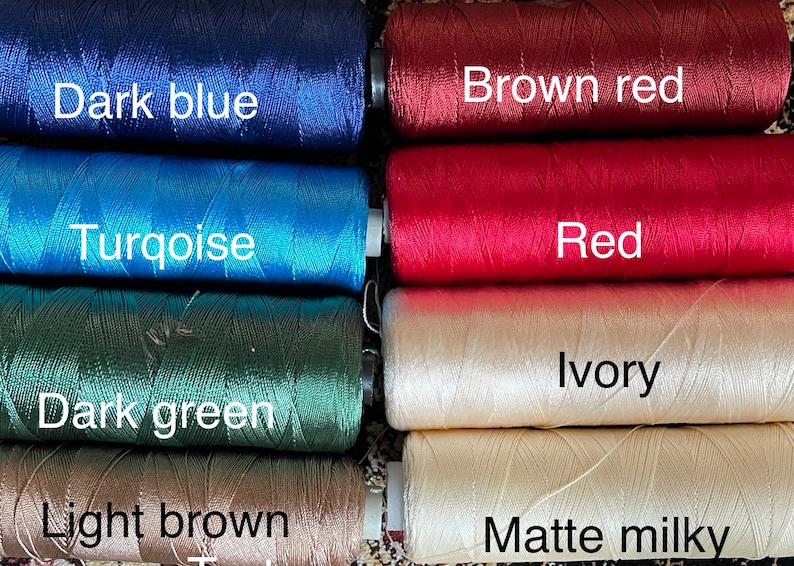 May include: Close-up of eight spools of thread in different colors. The colors are dark blue, turquoise, dark green, light brown, brown red, red, ivory, and matte milky.