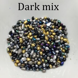 Op de afbeelding: Een mix van donker gekleurde sprinkles in verschillende vormen en maten. De sprinkles zijn goud, zilver, zwart en iriserend.
