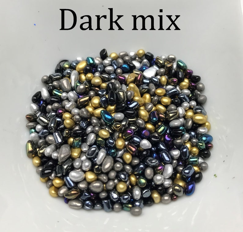 Op de afbeelding: Een mix van donker gekleurde sprinkles in verschillende vormen en maten. De sprinkles zijn goud, zilver, zwart en iriserend.