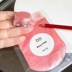 May include: A small clear jar filled with a pink powder labeled "DD Rosy Pink Net: 5g" in a clear plastic bag with a red pencil.