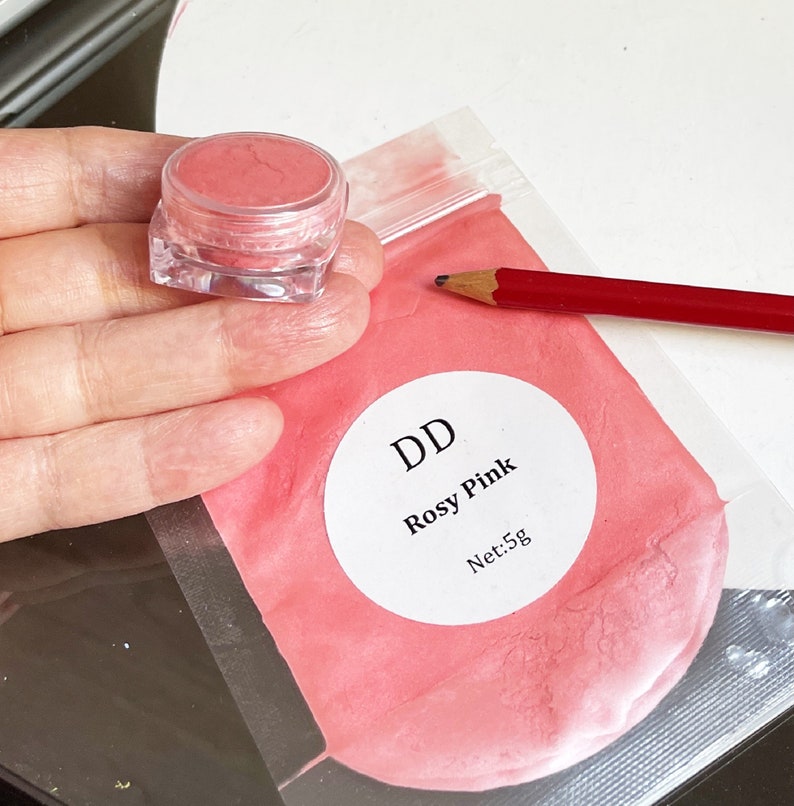 May include: A small clear jar filled with a pink powder labeled "DD Rosy Pink Net: 5g" in a clear plastic bag with a red pencil.