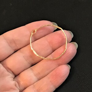 May include: A gold-toned, textured, circular metal hoop with a small opening. The hoop is about 2 inches in diameter.