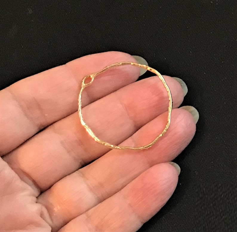 May include: A gold-toned, textured, circular metal hoop with a small opening. The hoop is about 2 inches in diameter.