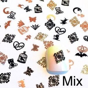 May include: Assortment of black and gold metal nail art charms. The charms include hearts, cages, butterflies, pumpkins, bats, stars, and crescent moons. The word "Love" is written on two of the hearts. The word "Mix" is written on the bottom right of the image.