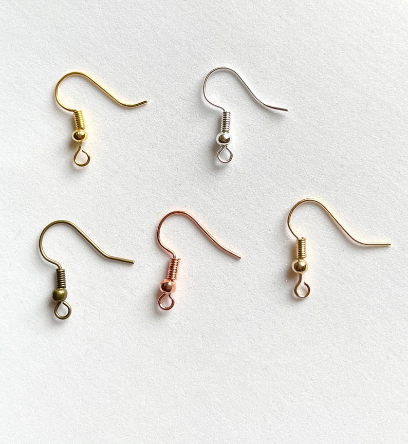 May include: Five earring hooks in different metal finishes: gold, silver, rose gold, and two shades of bronze. The hooks are all the same size and shape, with a small loop at the top and a ball at the bottom.