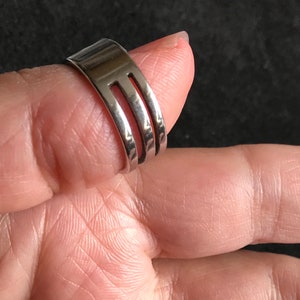 May include: A silver-colored ring made from a fork, with three tines visible. The ring is worn on a finger, showcasing the unique design and craftsmanship. The ring is a creative and unusual piece of jewelry.