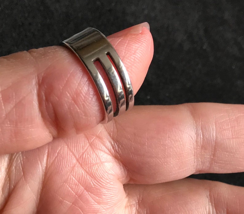 May include: A silver-colored ring made from a fork, with three tines visible. The ring is worn on a finger, showcasing the unique design and craftsmanship. The ring is a creative and unusual piece of jewelry.
