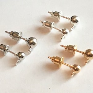 Op de afbeelding: Een set oorknopjes met een zilveren en gouden afwerking. De oorknopjes hebben een kleine bol aan het einde en een pin om oorbellen aan te bevestigen.